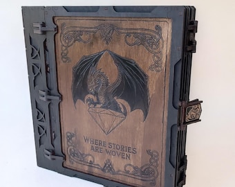May include: A wooden book-shaped box with a dragon and diamond design on the front. The box is dark brown with black accents and the text "WHERE STORIES ARE WOVEN". The box has a clasp closure.