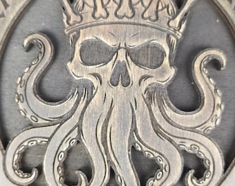 May include: A circular dark brown wooden plaque featuring a carved design of a skull wearing a crown made of bones, with octopus tentacles extending downwards. The text CAPTAIN'S LURK is carved at the top and LIBERTALIA is carved at the bottom.