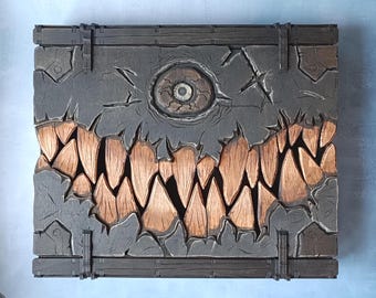 May include: A carved wooden wall art piece featuring a monster design. The artwork has a gray background with a large eye and a mouth full of sharp teeth in shades of brown. The piece is framed with dark wood.
