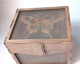May include: A wooden box with a carved butterfly design on the lid. The box is stained in shades of brown and features decorative corner details and a front clasp. The butterfly is intricately detailed, adding a touch of nature-inspired artistry.