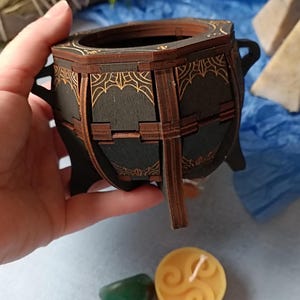 Gothic witchcraft-inspired wooden cauldron storage box, perfect for Wiccans, pagans, and fantasy lovers, handcrafted with engraved mystical symbols, aged wood finish for a dark academia aesthetic, ideal for storing tarot cards, spell ingredients, and enchanted trinkets, unique rustic altar decor piece, Halloween-themed gothic jewelry holder, handcrafted magical keepsake box, witchy home decor for occult and fantasy fans, rustic Wiccan potion holder, mystical spell storage chest