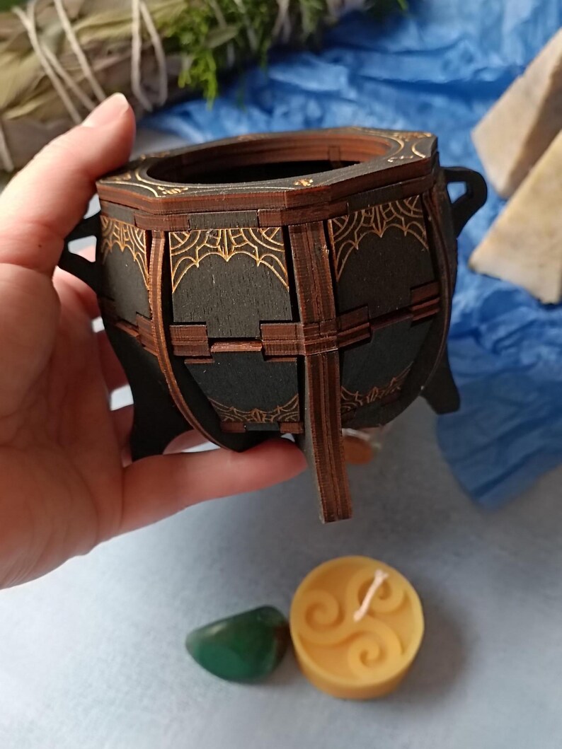Gothic witchcraft-inspired wooden cauldron storage box, perfect for Wiccans, pagans, and fantasy lovers, handcrafted with engraved mystical symbols, aged wood finish for a dark academia aesthetic, ideal for storing tarot cards, spell ingredients, and enchanted trinkets, unique rustic altar decor piece, Halloween-themed gothic jewelry holder, handcrafted magical keepsake box, witchy home decor for occult and fantasy fans, rustic Wiccan potion holder, mystical spell storage chest