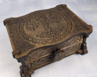 May include: A rectangular dark brown wooden box featuring an intricate laser-engraved tree of life design on the lid, surrounded by Celtic knotwork patterns. The front panel includes a circular knob with a triskelion symbol and matching knotwork.