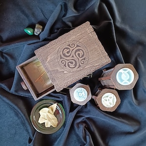 May include: A wooden box with a Celtic knot design on the lid. The box has a drawer that is open, revealing a small compartment. There are three small wooden boxes with Celtic knot designs on the lids. The boxes are on a black fabric surface.