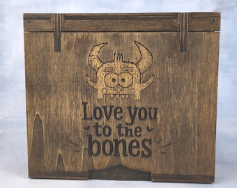 May include: A wooden box with a hinged lid and a dark brown finish. The box features a cartoon monster illustration and the phrase "Love you to the bones" engraved on the front.