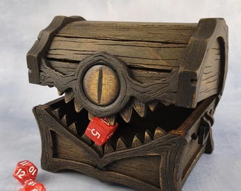 May include: A wooden treasure chest with an open lid, featuring a carved eye and jagged teeth design. The chest is brown with a distressed finish. Three red dice with white numbers are scattered around the chest, one inside the chest.