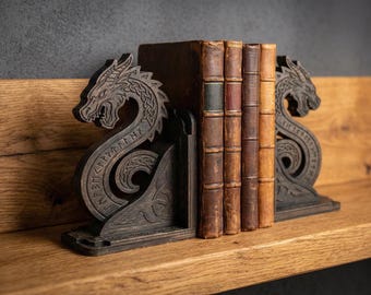 May include: A pair of dark brown wooden bookends featuring carved dragon heads and intricate knotwork patterns, with runic inscriptions along the curved bodies, supporting a row of four vintage leather-bound books with weathered spines.