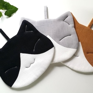 Può includere: Tre presine a forma di gatto in nero, grigio e marrone con accenti bianchi. Le presine sono realizzate in tessuto e hanno un design cucito.