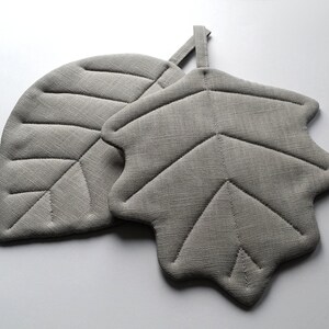 Puede incluir: Dos posavasos de hoja de lino gris. Los posavasos est&aacute;n acolchados con un dise&ntilde;o de hoja.