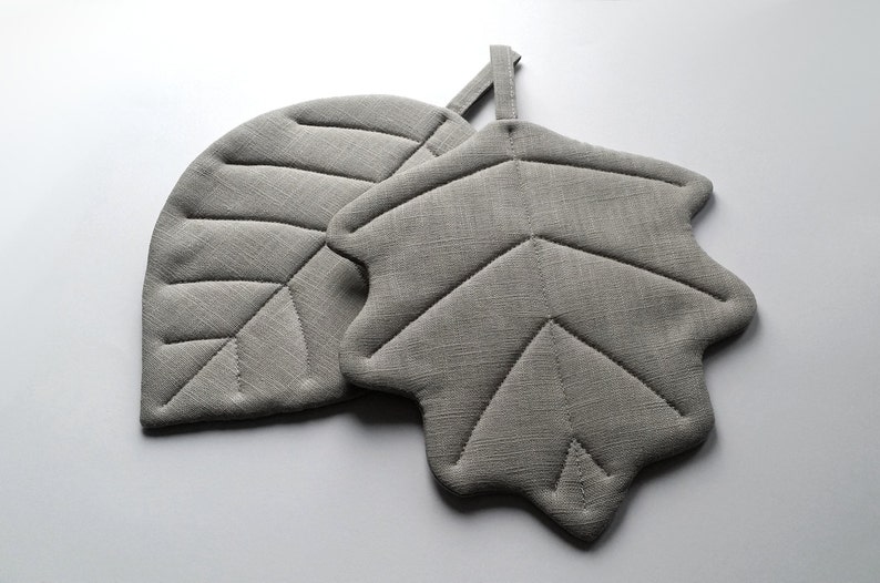 Puede incluir: Dos posavasos de hoja de lino gris. Los posavasos est&aacute;n acolchados con un dise&ntilde;o de hoja.