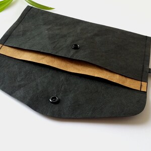 Puede incluir: Un clutch negro estilo sobre con un acento marr&oacute;n y cierres de bot&oacute;n a presi&oacute;n. El clutch est&aacute; hecho de un material texturizado y tiene un dise&ntilde;o simple y minimalista. Adecuado para llevar objetos peque&ntilde;os.