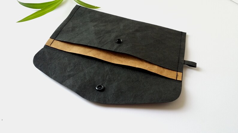 Puede incluir: Un clutch negro estilo sobre con un acento marr&oacute;n y cierres de bot&oacute;n a presi&oacute;n. El clutch est&aacute; hecho de un material texturizado y tiene un dise&ntilde;o simple y minimalista. Adecuado para llevar objetos peque&ntilde;os.
