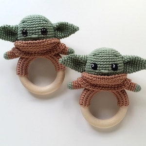 May include: Two crocheted green and brown baby rattles with wooden rings. The rattles are shaped like a popular fictional character.