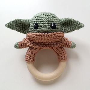 May include: A crocheted green and brown baby rattle shaped like a character from Star Wars. The rattle has a wooden ring and is a great toy for babies.