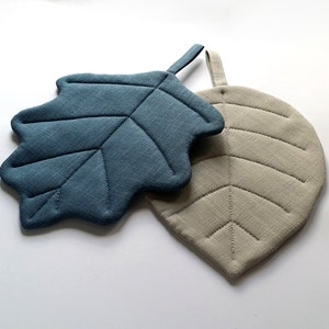 Puede incluir: Dos posavasos con forma de hoja, uno azul y otro beige, con un dise&ntilde;o acolchado. El posavasos azul tiene un asa de bucle.