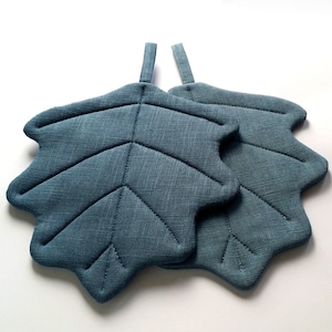 Puede incluir: Dos agarraderas de olla de hoja azul acolchadas con un lazo para colgar.