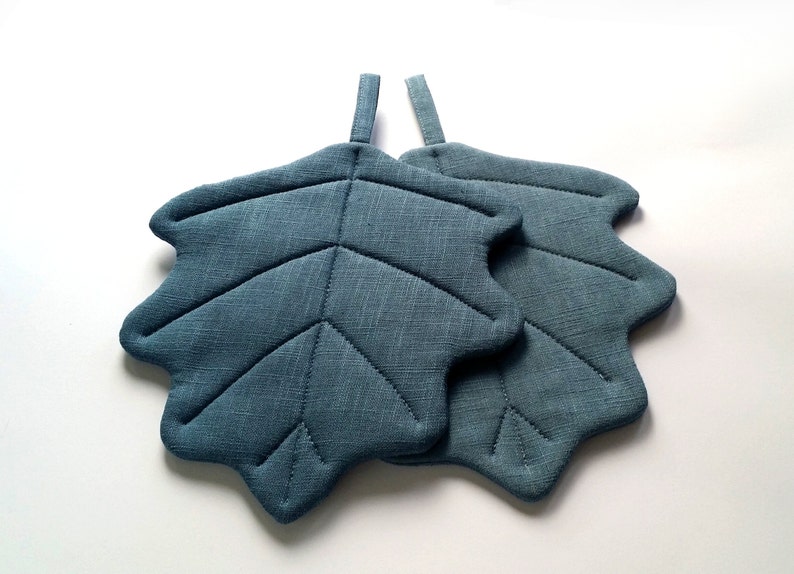 Puede incluir: Dos agarraderas de olla de hoja azul acolchadas con un lazo para colgar.