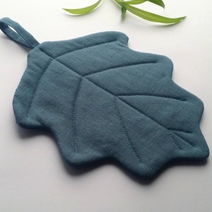 Puede incluir: Un posavasos en forma de hoja de color azul verdoso con un asa de bucle. El posavasos est&aacute; acolchado con un dise&ntilde;o de hoja.