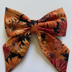 May include: A large black bow with a sunflower print in shades of orange, red, and gold. The bow is made of fabric and has a pointed shape.