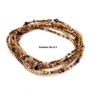 May include: A set of three beaded waist beads in shades of gold, brown, and purple. The beads are small and strung together, forming multiple strands. The text "Goddess Set of 3" is displayed.