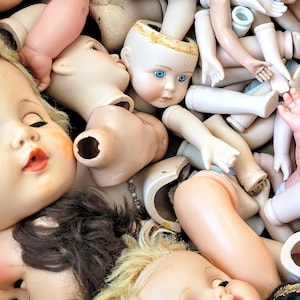May include: A collection of vintage porcelain doll heads and body parts in various poses. The dolls are mostly white with some painted details, and some have blue eyes.