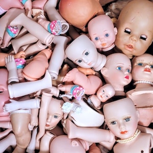 May include: A collection of vintage porcelain dolls with various painted facial features and hairstyles. The dolls are in various poses and have different outfits, including dresses, pants, and shirts.
