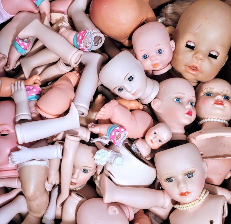 May include: A collection of vintage porcelain dolls with various painted facial features and hairstyles. The dolls are in various poses and have different outfits, including dresses, pants, and shirts.