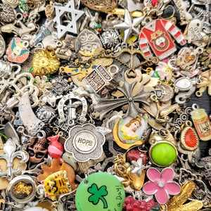 May include: A large collection of colourful charms and pendants, including a star, a cross, a horseshoe, a heart, a crown, a butterfly, a flower, a shamrock, a skull, a cat, a princess, and a bottle of Duff beer. The charms are made of metal, glass, and plastic.