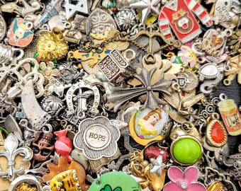 May include: A large collection of colorful charms and pendants, including a star, a cross, a horseshoe, a heart, a crown, a butterfly, a flower, a shamrock, a skull, a cat, a princess, and a bottle of Duff beer. The charms are made of metal, glass, and plastic.
