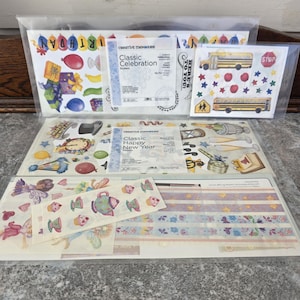 Puede incluir: Una colección de pegatinas Creative Memories en envases de plástico transparente. Las pegatinas presentan temas de cumpleaños, escolares y festivos. El texto del embalaje dice "Classic Celebration" y "Classic Happy New Year".