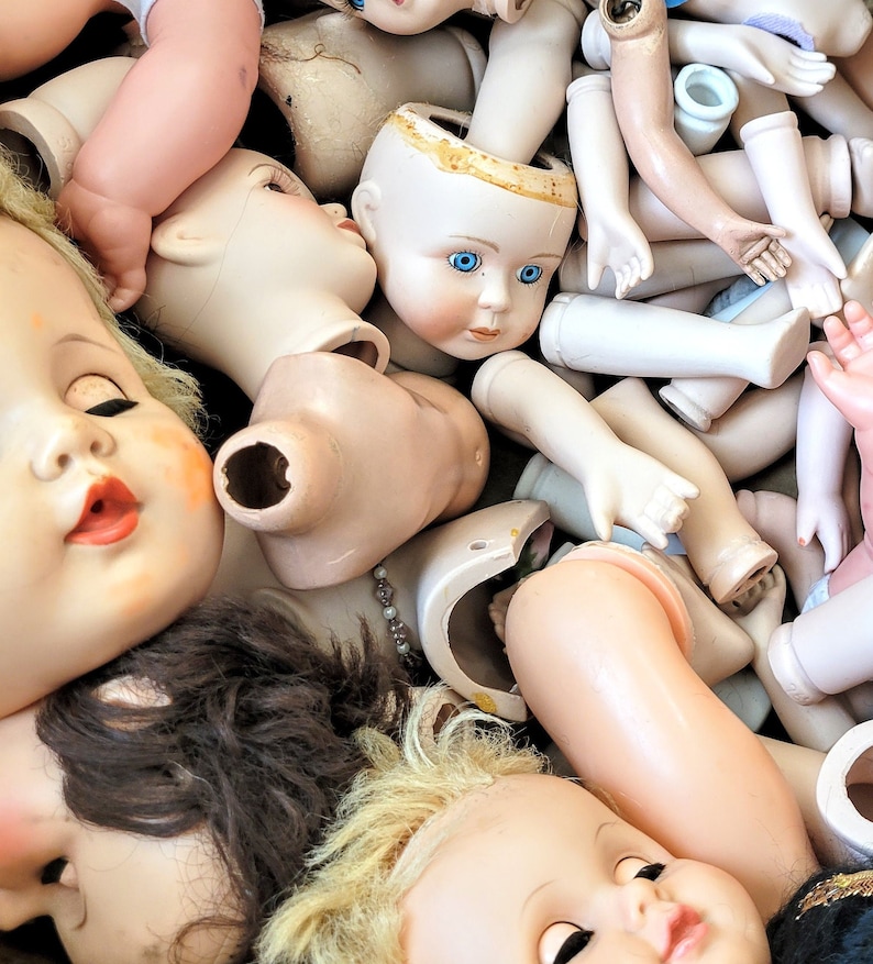 May include: A collection of vintage porcelain doll heads and body parts in various poses. The dolls are mostly white with some painted details, and some have blue eyes.