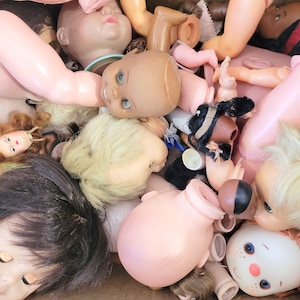 May include: A collection of vintage porcelain dolls with painted faces and various hairstyles. The dolls are in various poses and have different colored dresses and outfits.