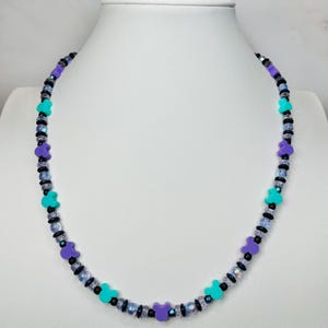 May include: A beaded necklace with a playful design. The necklace features alternating beads in black, iridescent, and small turquoise and purple Mickey Mouse-shaped beads. The necklace is displayed on a white mannequin.