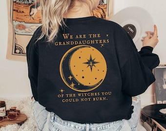 Może przedstawiać: Czarna bluza z złotym tekstem i grafiką. Tył bluzy zawiera napis "We are the granddaughters of the witches you could not burn". Złoty półksiężyc i grafika gwiazdy są wyśrodkowane pod tekstem.