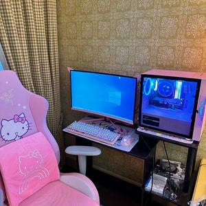 May include: A pink gaming chair with a Hello Kitty design, a black desk with a pink keyboard, a curved monitor, and a pink computer tower with RGB lighting.