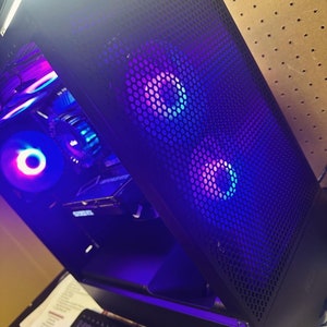 May include: A black computer case with a mesh side panel. The case has two fans with blue and purple LED lights. The fans are visible through the mesh panel.