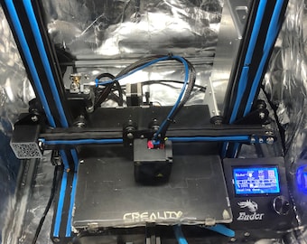 May include: A black 3D printer with a blue and black frame. The printer is inside a silver reflective enclosure. The printer's display shows the text "Ender" and "Heating done".