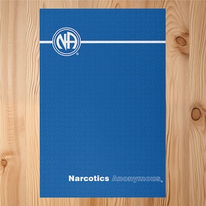 Puede incluir: Un rompecabezas azul con el logotipo de Narcóticos Anónimos en blanco. El logotipo es un círculo con las letras "NA" en su interior y una línea horizontal blanca. Las palabras "Narcóticos Anónimos" están impresas en blanco en la parte inferior.