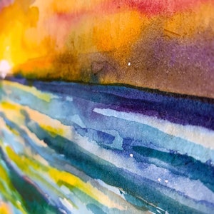 Op de afbeelding: Abstracte aquarelverf met een levendige zonsondergangshemel in tinten oranje, geel, roze en paars. De onderkant van het schilderij heeft een reeks blauwe, groene en gele horizontale penseelstreken, die lijken op water.