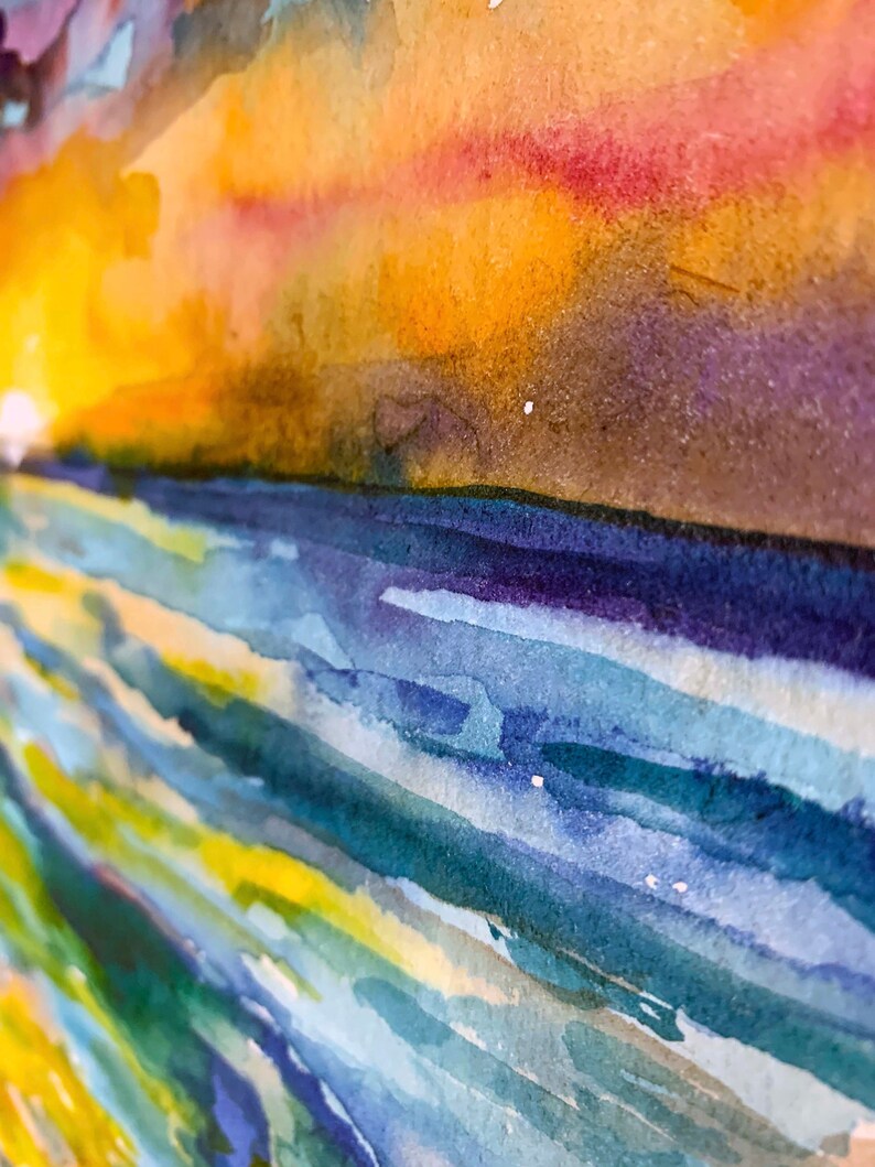 Op de afbeelding: Abstracte aquarelverf met een levendige zonsondergangshemel in tinten oranje, geel, roze en paars. De onderkant van het schilderij heeft een reeks blauwe, groene en gele horizontale penseelstreken, die lijken op water.