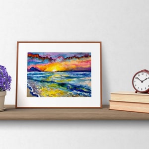 Op de afbeelding: Een ingelijst aquarel schilderij van een zonsondergang boven de oceaan. De lucht is een mix van paars, roze en oranje, met wolken die de kleuren reflecteren. De oceaan is diepblauw, met golven die breken op de kust. Het zand is lichtgeel.