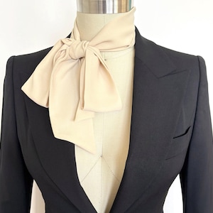 May include: A black blazer with a large, cream-colored bow tie.