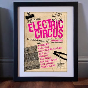 May include: A framed concert poster for the Electric Circus in Manchester, dated October 1977. The poster features bright pink text on a beige background, with graphics of a black binder clip, safety pins, and a zipper. It lists bands like Buzzcocks.