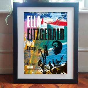 Puede incluir: Póster enmarcado con Ella Fitzgerald, con el texto "Ella Fitzgerald Live in Chicago". El póster tiene un fondo abstracto colorido con un retrato de Fitzgerald y micrófonos.