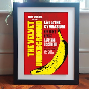Könnte beinhalten: Ein gerahmtes Poster mit einer gelben Banane auf rotem Hintergrund und weißem sowie gelbem Text: ANDY WARHOL PRESENTS THE VELVET UNDERGROUND LIVE AT THE GYMNASIUM NEW YORK'S NEWEST HAPPENING DISCOTHEQUE EVERY FRIDAY, SATURDAY AND SUNDAY FROM 9PM 424 EAST 71ST STREET.