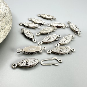 May include: A collection of silver-toned jewelry clasps with intricate floral designs. One clasp is stamped with "JAPAN". The clasps are oval-shaped with a hook and eye closure, perfect for necklaces or bracelets.