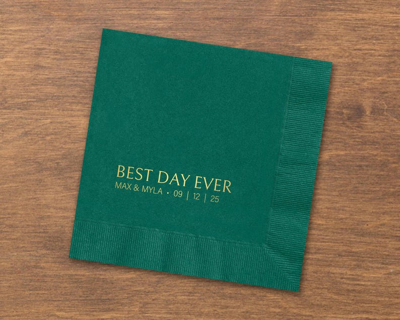 May include: A square dark green paper napkin featuring gold foil text that reads BEST DAY EVER followed by the names MAX & MYLA and the date 09 | 12 | 25. The napkin has a textured border along the right edge and a smooth center surface.