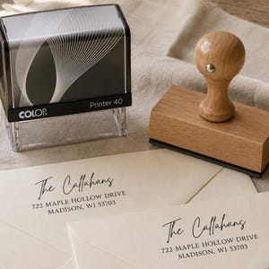 May include: A black self-inking Colop Printer 40 stamp and a wooden handle rubber stamp. Both stamps are positioned above two cream-colored envelopes, each printed with the address: The Callahans, 722 Maple Hollow Drive, Madison, WI 53703.