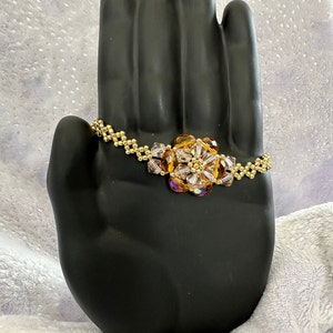 May include: A gold beaded bracelet with a flower-shaped charm made of clear and amber glass beads.