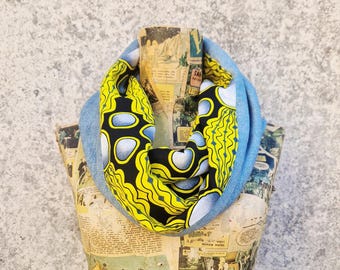 May include: A blue denim infinity scarf featuring a bold yellow, black, and white patterned fabric. The scarf is presented on a mannequin adorned with vintage comic strips, against a grey backdrop.